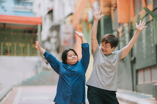 happy asian malay autism down syndrome female  enjoy dancing with her female friend in city street